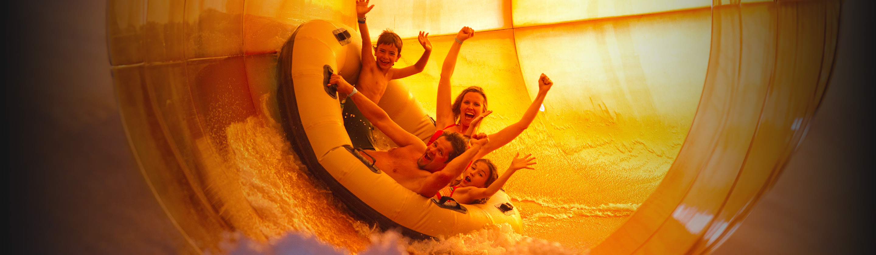 Image of family of 4 riding a yellow waterslide on a yellow inflatable raft